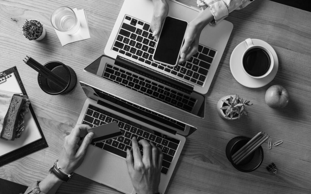 Two people on laptops with phones and credit cards