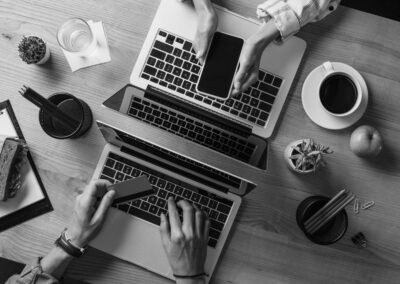 Two people on laptops with phones and credit cards