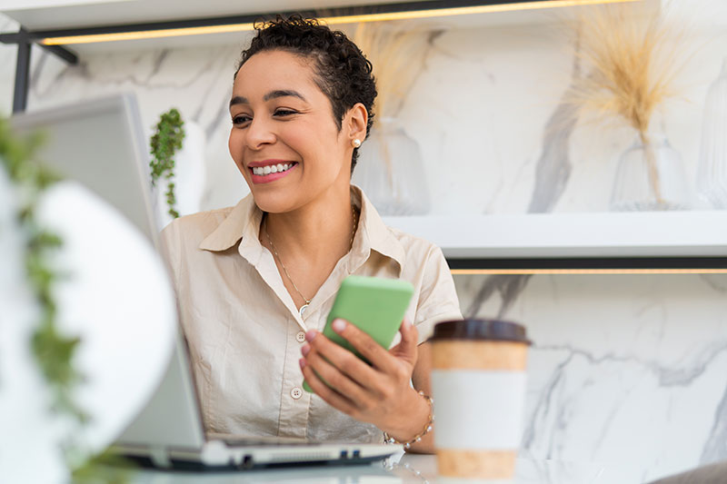 Woman holding phone in one hand while working on laptop